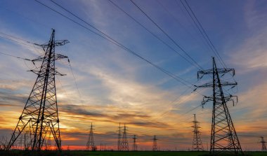 Yüksek voltajlı elektrik hatlarının silueti gün doğumunda ya da günbatımında renkli bir gökyüzüne karşı.