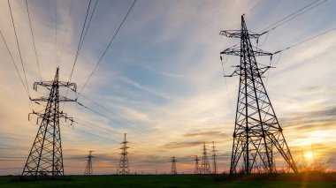 Yüksek voltajlı elektrik hatlarının silueti gün doğumunda ya da günbatımında renkli bir gökyüzüne karşı.
