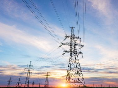 Yüksek voltajlı elektrik hatlarının silueti gün doğumunda ya da günbatımında renkli bir gökyüzüne karşı.