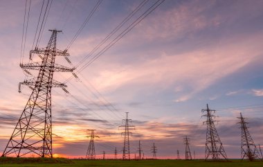 Yüksek voltajlı elektrik hatlarının silueti gün doğumunda ya da günbatımında renkli bir gökyüzüne karşı.
