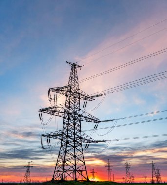 Yüksek voltajlı elektrik hatlarının silueti gün doğumunda ya da günbatımında renkli bir gökyüzüne karşı.