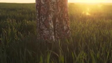 Çiçekli etekli bir kız Sunset 'te bir tarlada yürüyor.