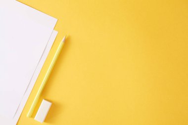 Sarı kalem, beyaz kağıtlar ve silgi. Sarı arkaplanda metin veya çizim için boş yer.