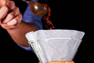 Elleri filtrede öğütülmüş kahveyi su ısıtıcısına döküyor. Alternatif kahve demlemeye hazırlanıyorum. Elinde kaşık, elinde öğütülmüş kahveyle...