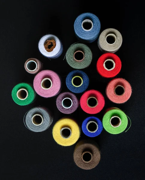 colorful spools of thread top view on black background