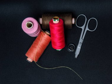 Siyah arkaplanda iplikler ve düğmeler dikiliyor