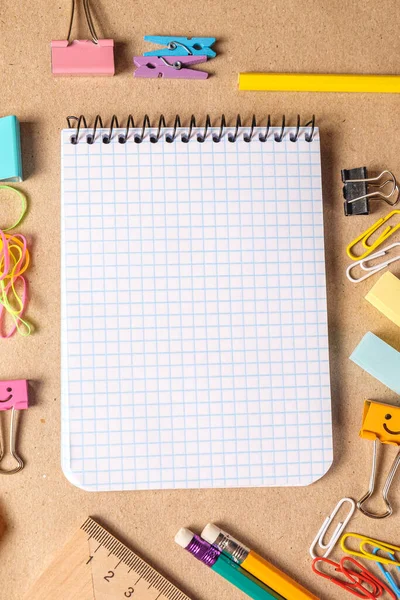 On a desk with pens and accessories to draw a copybook .Cell lined pages copybook with metal spiral template and Colored office supplies on brown craft paper background. School office supplies. Top viev.