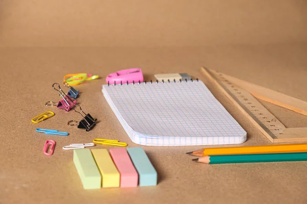 On a desk with pens and accessories to draw a copybook .Cell lined pages copybook with metal spiral template and Colored office supplies on brown craft paper background. School office supplies. Top viev.