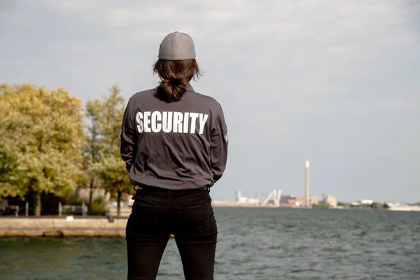 A female security guard in uniform and mask watching over the harbor area.