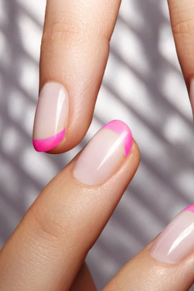 Händerna med rosa fransk manikyr. Spikar konst design. Närbild av händer med trendiga neonnaglar på randigt tryck — Stockfoto