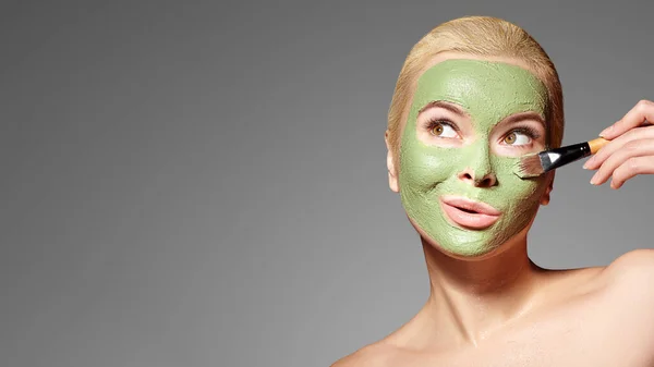 Beautiful Woman Applying Green Facial Mask. Beauty Treatments. Spa Girl Apply Clay Facial mask on grey background — Stock Photo, Image