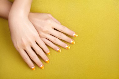 Beautiful Female Hands with bright Orange Manicure like Candy Corn on Yellow Background. Manicured Nails with Creative Gel Polish Design. Halloween Style