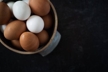 Üst Manzara. Koyu arkaplanda taze kahverengi ve beyaz yumurtalardan oluşan el yapımı seramik bir kase düz görünüm sergile. Yüksek kalite fotoğraf. Çok basit. Sağlıklı. Pişirme, pişirme. Karışık yumurta..