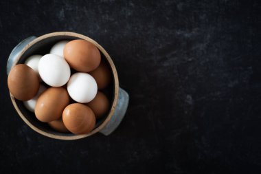 Üst Manzara. Koyu arkaplanda taze kahverengi ve beyaz yumurtalardan oluşan el yapımı seramik bir kase düz görünüm sergile. Yüksek kalite fotoğraf. Çok basit. Sağlıklı. Pişirme, pişirme. Karışık yumurta..