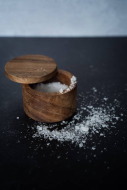 Koyu huysuz arka planda, ahşap tuz kabındaki organik deniz tuzu yığınının yan görüntüsü. Yüksek kalite fotoğraf. Çok basit. Sağlıklı. Pişirme, pişirme.