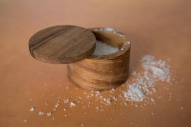 Turuncu terasotta arka planındaki ahşap tuz kabının içindeki organik deniz tuzu yığınının en üst görüntüsü. Yüksek kalite fotoğraf. Çok basit. Sağlıklı. Pişirme, pişirme.