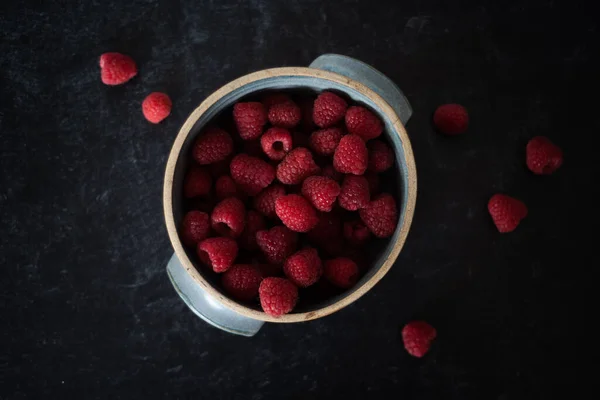 Bowl of raspberries in blue ceramic pot on dark background. High quality photo. Handmade ceramic bowl. Lay flat view. Top down view.