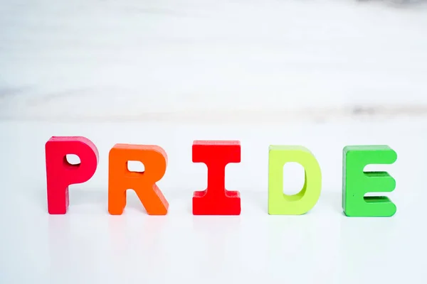 Word pride in colored block lettering with colored rainbow shapes in background. High quality photo. Love is love. Celebrating pride.