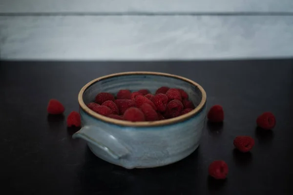 Bowl of raspberries in blue ceramic pot on dark background. High quality photo. Handmade ceramic bowl.