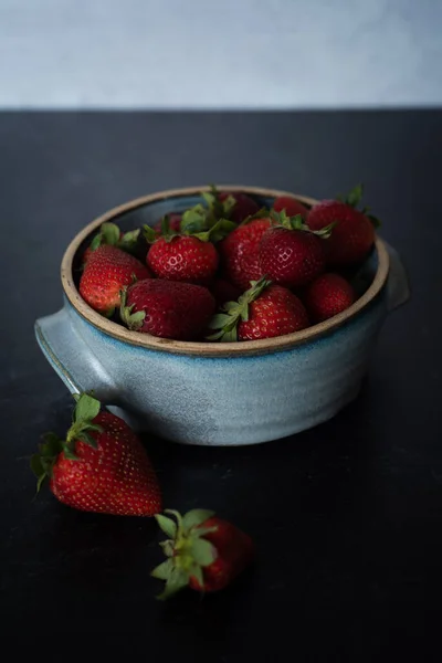 Bowl of raspberries in blue ceramic pot on dark background. High quality photo. Handmade ceramic bowl. Fresh summer fruit spilling out of bowl. Vibrant colors.