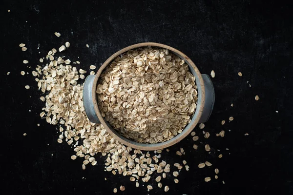 Top view of handmade ceramic bowl of organic oats on dark background.. High quality photo. Simple. Healthy. Cooking, baking. Organic oats breakfast. Blue ceramic bowl.