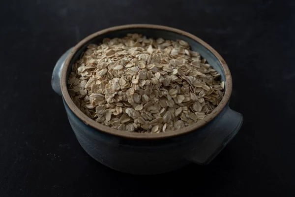 Top view of handmade ceramic bowl of organic oats on dark background with concrete wall. High quality photo. Simple. Healthy. Cooking, baking. Organic oats breakfast. Blue ceramic bowl.