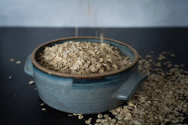 Top view of handmade ceramic bowl of organic oats on dark background with concrete wall. High quality photo. Simple. Healthy. Cooking, baking. Organic oats breakfast. Blue ceramic bowl. Oats poured.