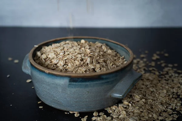 Top view of handmade ceramic bowl of organic oats on dark background with concrete wall. High quality photo. Simple. Healthy. Cooking, baking. Organic oats breakfast. Blue ceramic bowl.