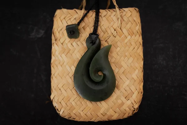 Pounamu fish hook necklace on dark background. Aotearoa, Maori. The fish hook denotes the importance of fishing to the Maori people of NZ and their strong relationship to Tangaroa, the god of the sea.