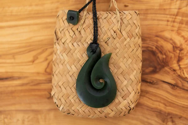Pounamu fish hook necklace on wooden background. Aotearoa, Maori. The fish hook denotes the importance of fishing to the Maori people of NZ and their strong relationship to Tangaroa, god of the sea.