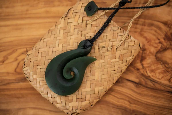 Pounamu fish hook necklace on wooden background. Aotearoa, Maori. The fish hook denotes the importance of fishing to the Maori people of NZ and their strong relationship to Tangaroa, god of the sea.