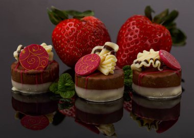 El yapımı yuvarlak çikolata ve beyaz çilek tatlısı ve naneli çikolata jöleli çikolata arkaplanda olgun kırmızı çilekler yansımalı siyah bardakta duruyor..