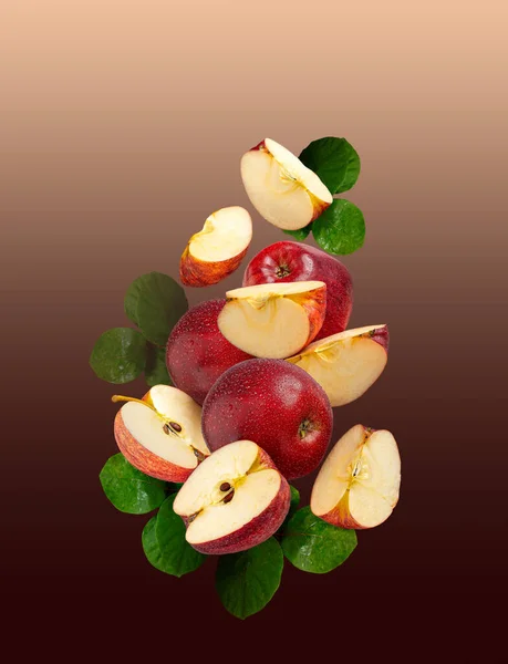 ripe whole red apples with cut slices, with green leaves on a gradient beige-brown background hanging in the air.