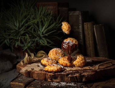 Eski tarz bir hayat. Hindistan cevizli kurabiyeler, büyük tahta bir kesikle havada asılı. Koyu ahşap bir masada, arka planda kitaplar ve çiçeklerle..