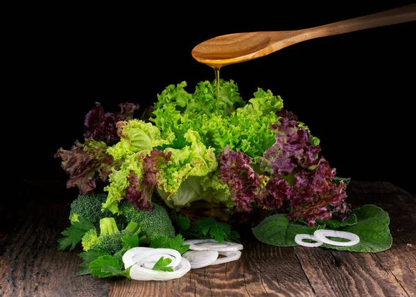 green leaf salad coral lettuce, curly endive with onion on a dark wooden table and olive oil