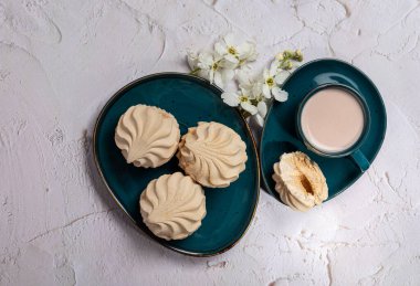 fresh soft milky-colored marshmallow with a dark blue-green filling, lying on a dish against a light structural background. a cup of cocoa Apple branch. View from above