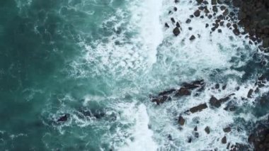 Güneşli bir günde, kayalara vuran dalgalarla sahilin insansız hava görüntüsü.