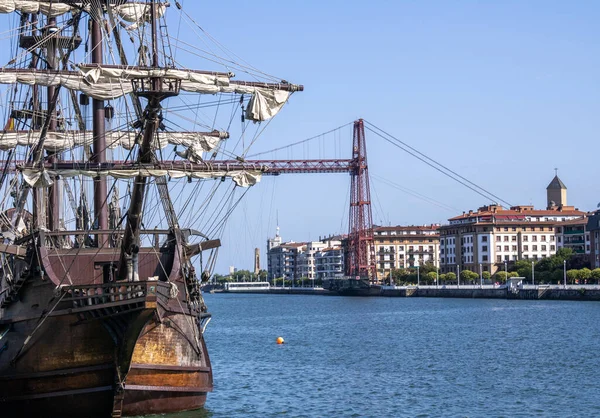 old wooden boat moored at the pier with the Bizkaia suspension bridge in the background and calm sea.