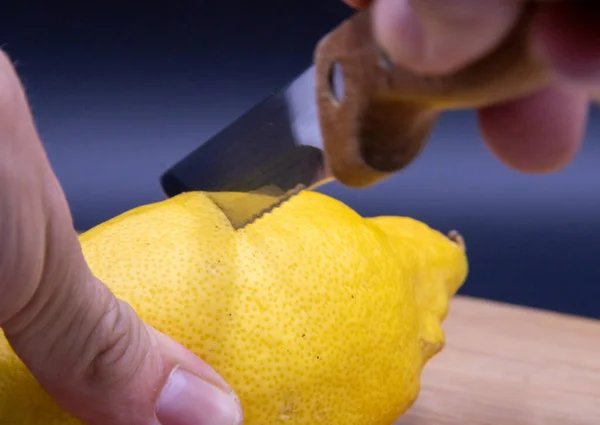 Siyah arka planda kesme tahtasında bıçakla limon kesen adamın elleri