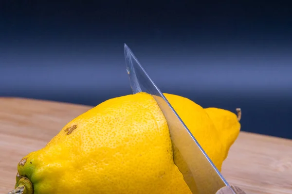 Siyah arka planda kesme tahtasında bıçakla limon kesen adamın elleri