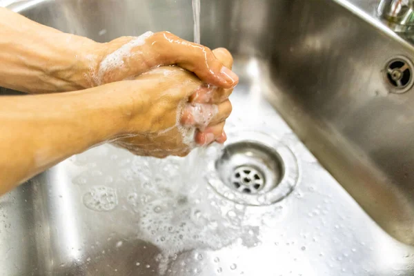 person washing hands with soap in kitchen sink