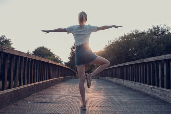 close-up of girl exercising on wooden bridge. Tranquility at sunset.