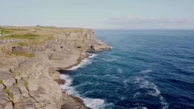 Güneşli bir günde, arka planda köyle birlikte dalgaların kayalara çarptığı Cantabrian kıyılarının insansız hava görüntüsü..