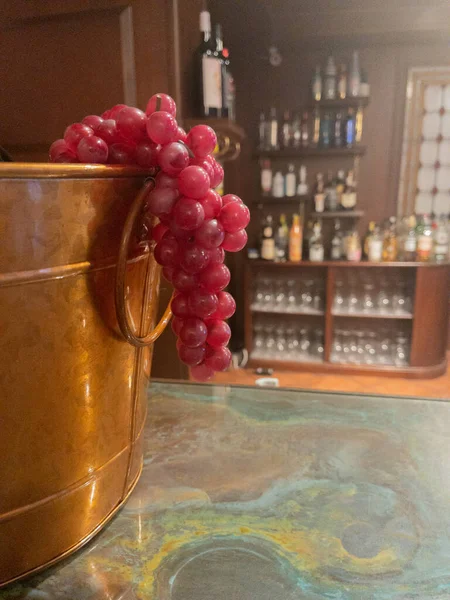 wine bucket with bunch of red grapes hanging with bottles in the background