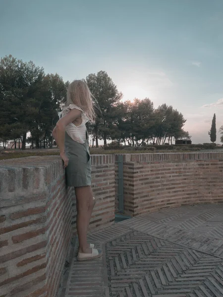 Woman leaning against a brick wall enjoying the sunset in a green dress