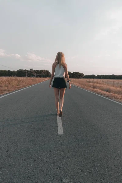 blonde-haired woman walking on the road at sunset in shorts