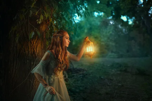 Fantasia elfo princesa mulher caminha na floresta escura noite, segurando lanterna brilhante nas mãos. Menina fada ruiva. Verão natureza floresta árvore verde. Cabelo vermelho longo, orelhas de elfo pontiagudas, vestido vintage medieval — Fotografia de Stock