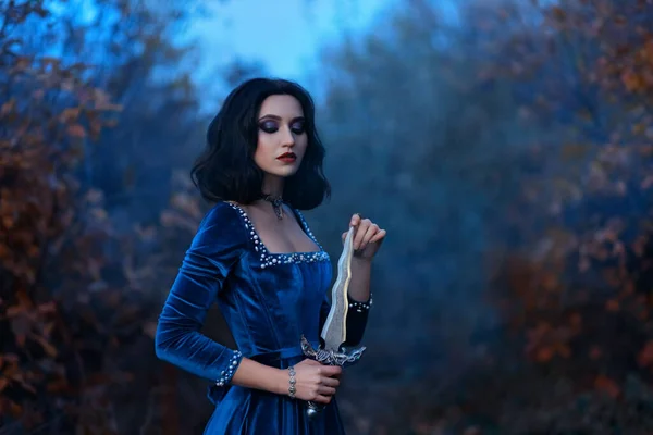 幻想中的中世纪女战士女王手持匕首，手持刀。皇家天鹅绒复古蓝色礼服珍珠，女公主吸血鬼，黑发短发。自然森林黄昏的夜晚，秋天的季节 — 图库照片