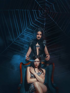Tahtta oturan fantezi kraliçesi. Seksi gümüş elbise. Gotik kötü cadı, ağ örüyor. Gotik bir görünüm. İblis örtüleri gözlerine dokunur. Örümcek ağlı kız prenses, pençeli eller. Cadılar Bayramı