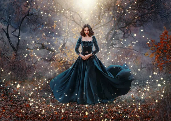 Gotico fantasia donna strega tenendo le mani libro di magia. Lungo velluto nero medievale abito vintage vola vento. La ragazza evoca. Luminosa luce divina bagliore scintilla cerchio magico intorno alla signora. Albero foresta autunnale. — Foto Stock